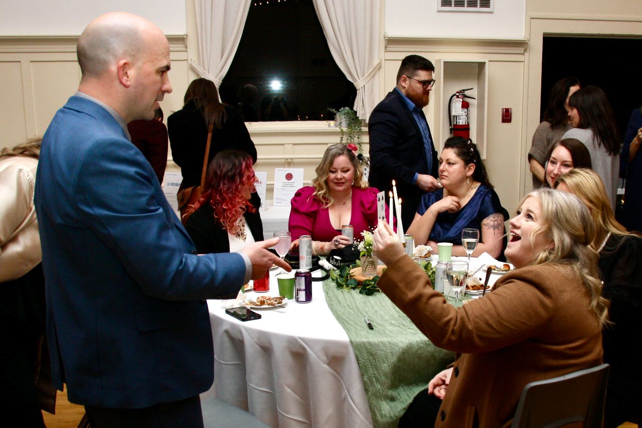 Geo performs close-up magic at a reception table as a guest holds her selected card in surprise